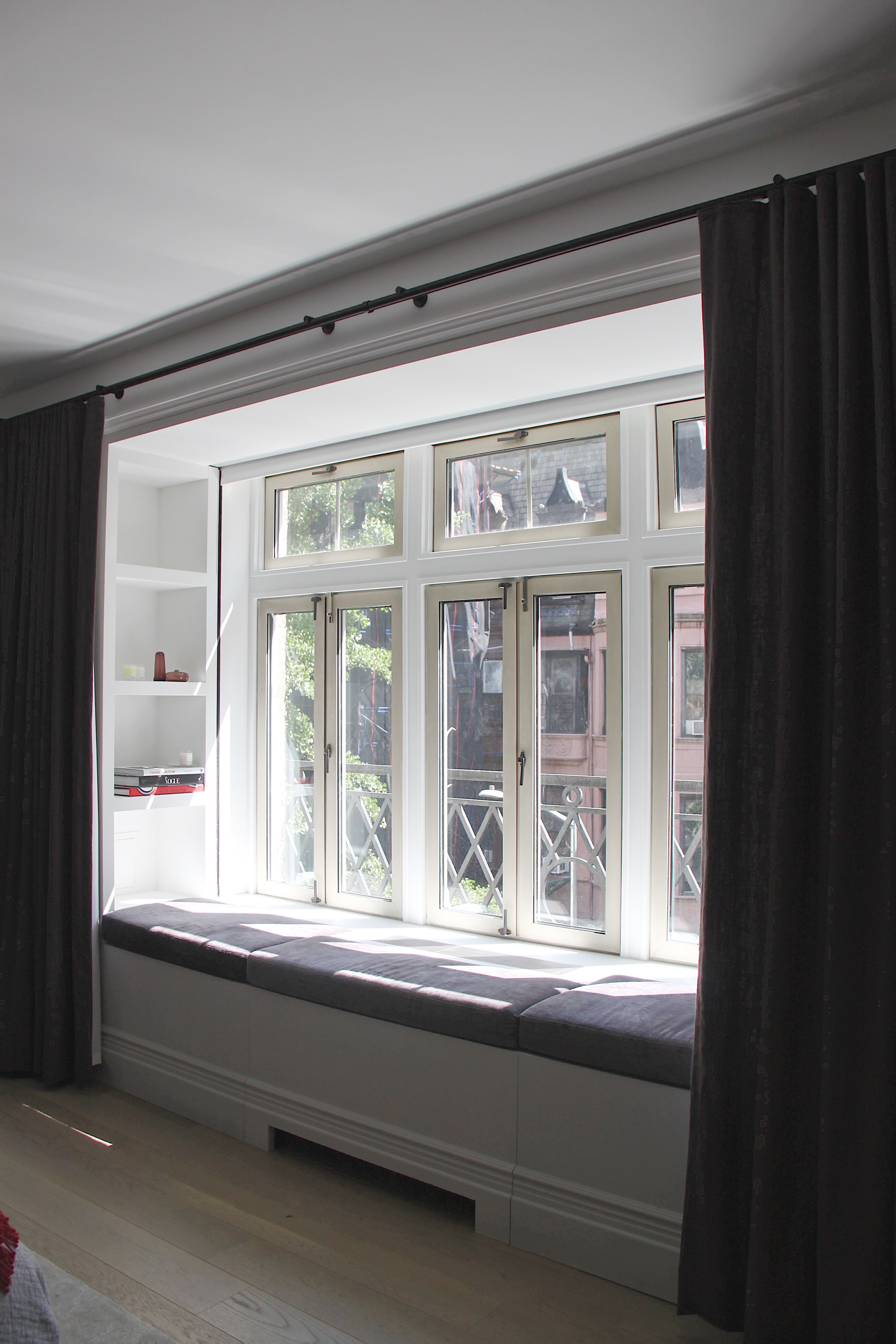 A window seat in a room with deep aubergine silk wallcoverings, wood millwork, and stone paneling. Fluted glass doors allow natural light in.