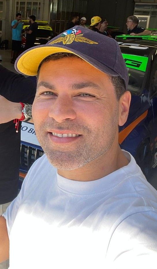 Retrato de Kleber Bertoldo, sorrindo, de boné e camiseta branca