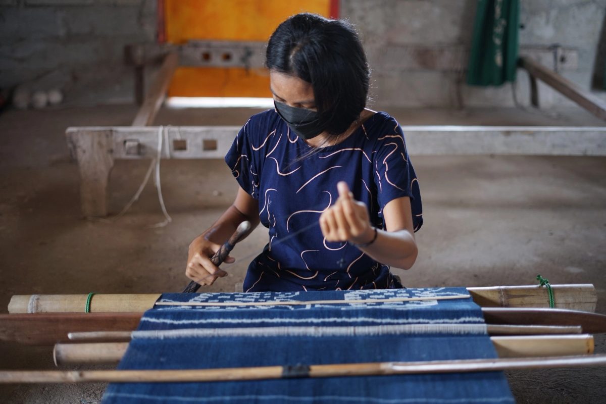 A woman weaving indigo cloth on a backstrap loom