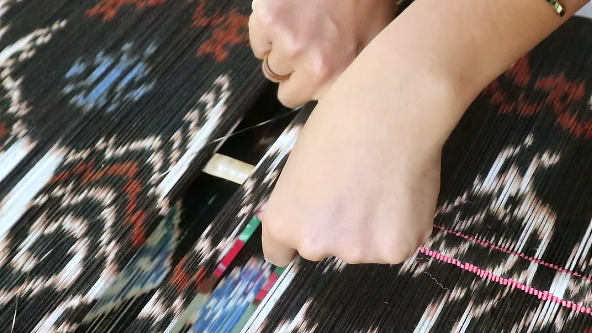 Hands securing patterned threads along a bamboo rod