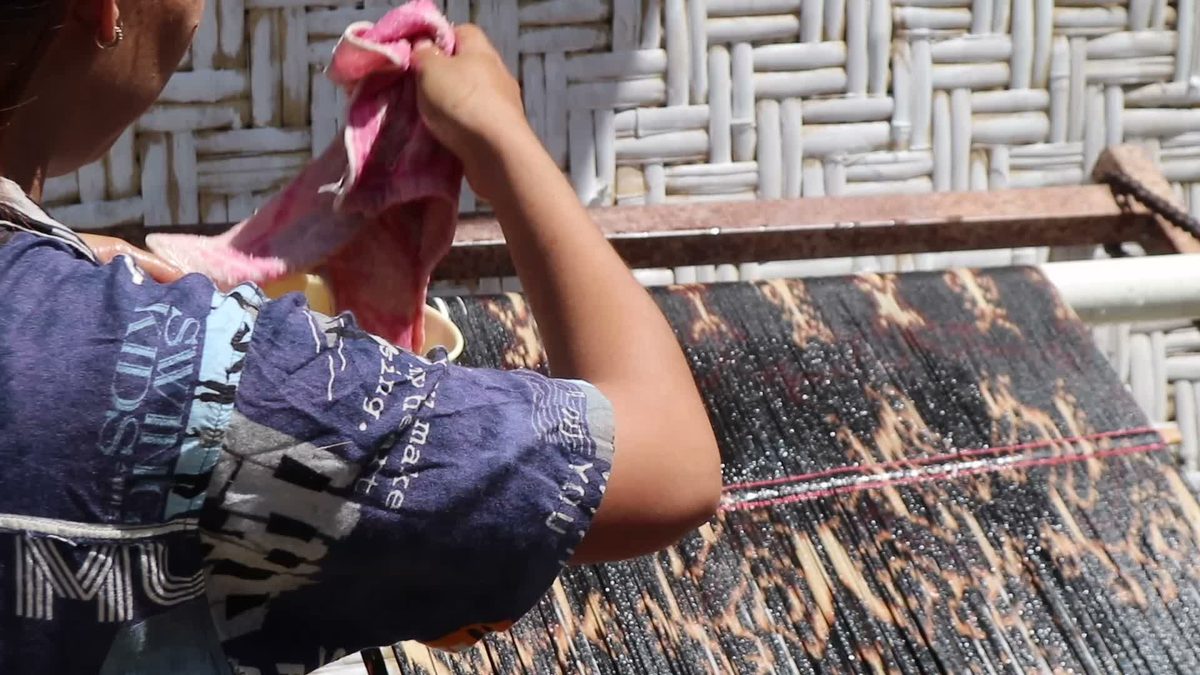 A woman applying starch to patterned warp threads