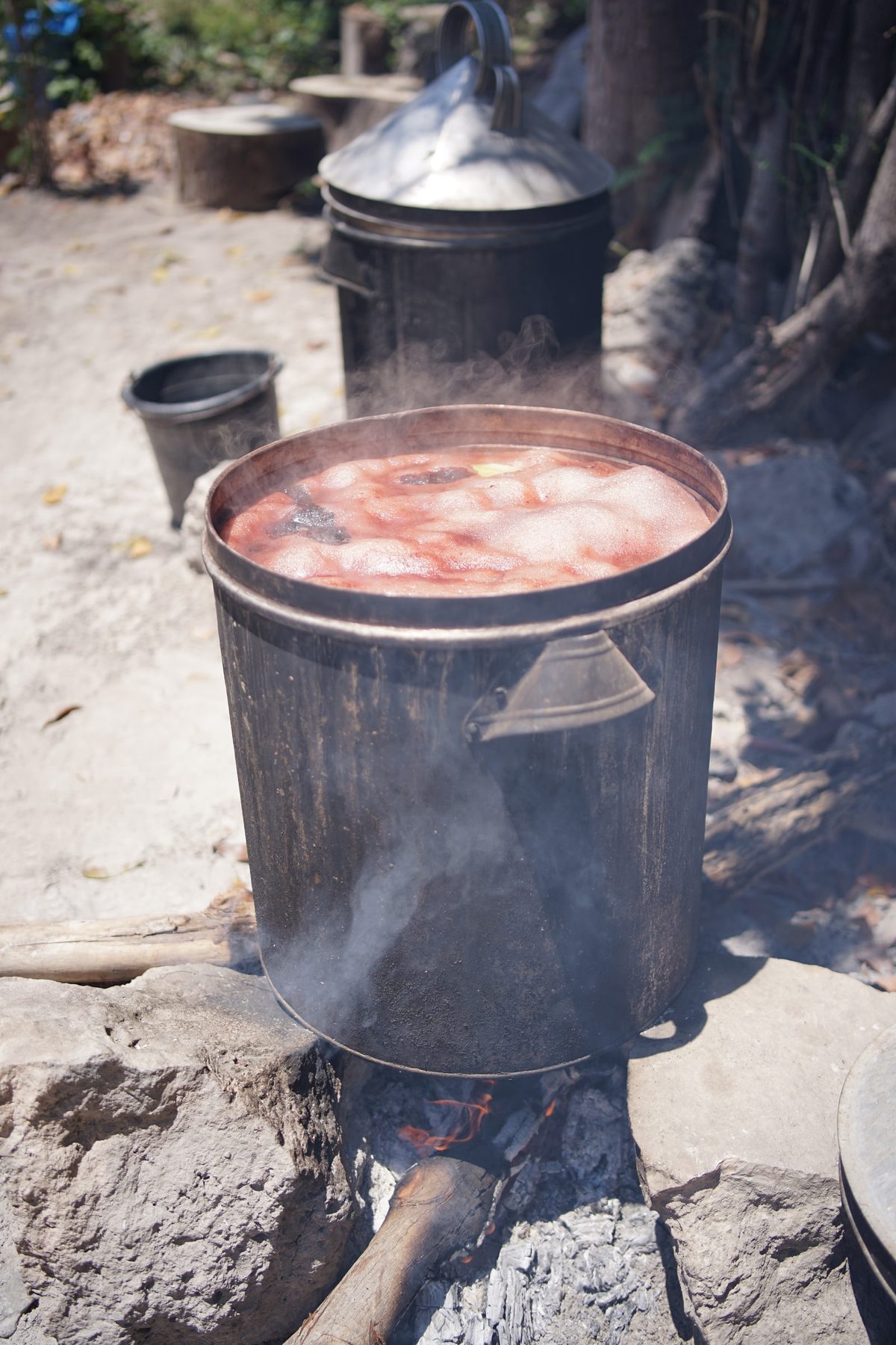 A pot of reddish natural dye heating over a wood fire
