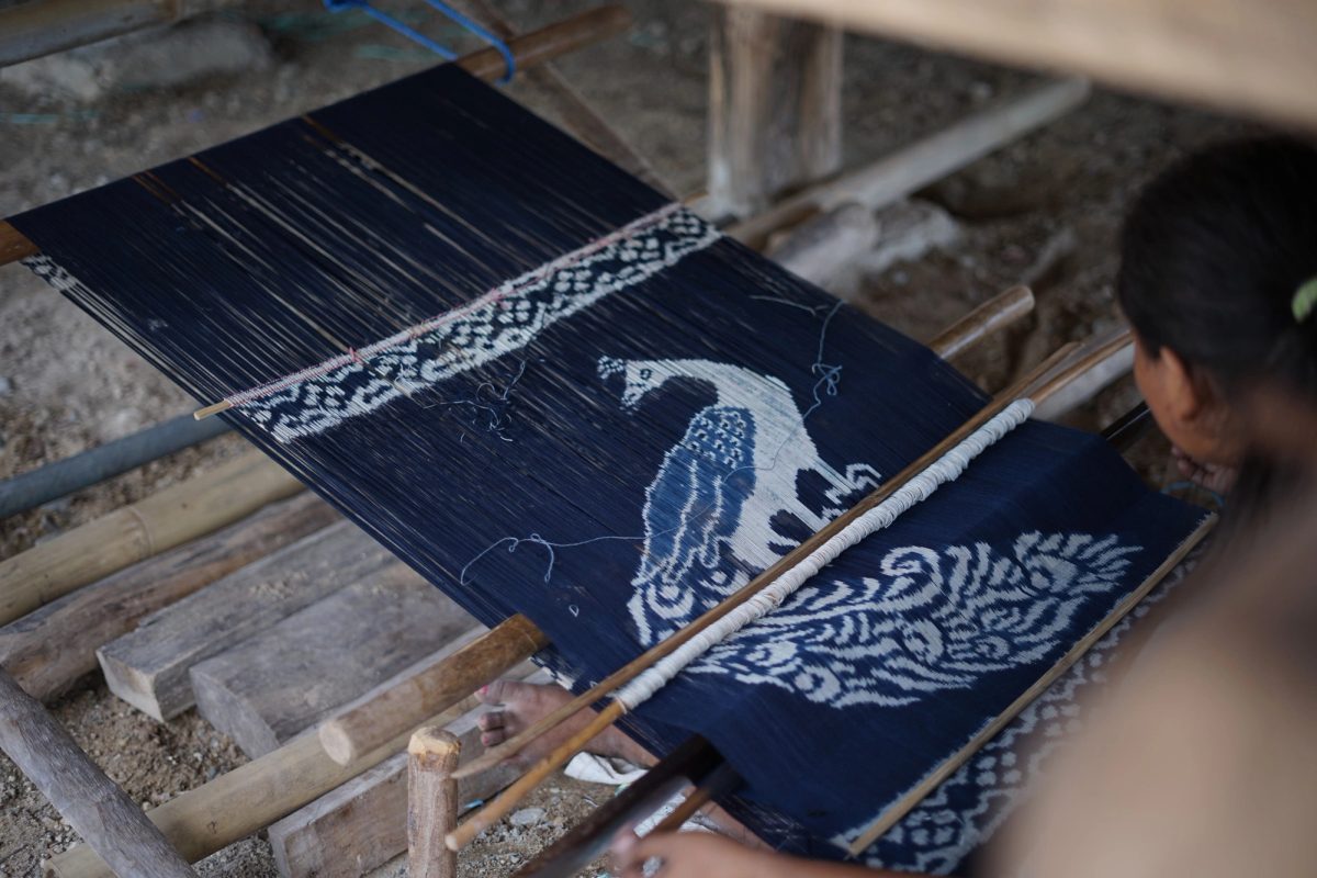 An indigo textile with a white bird motif taking shape on the loom