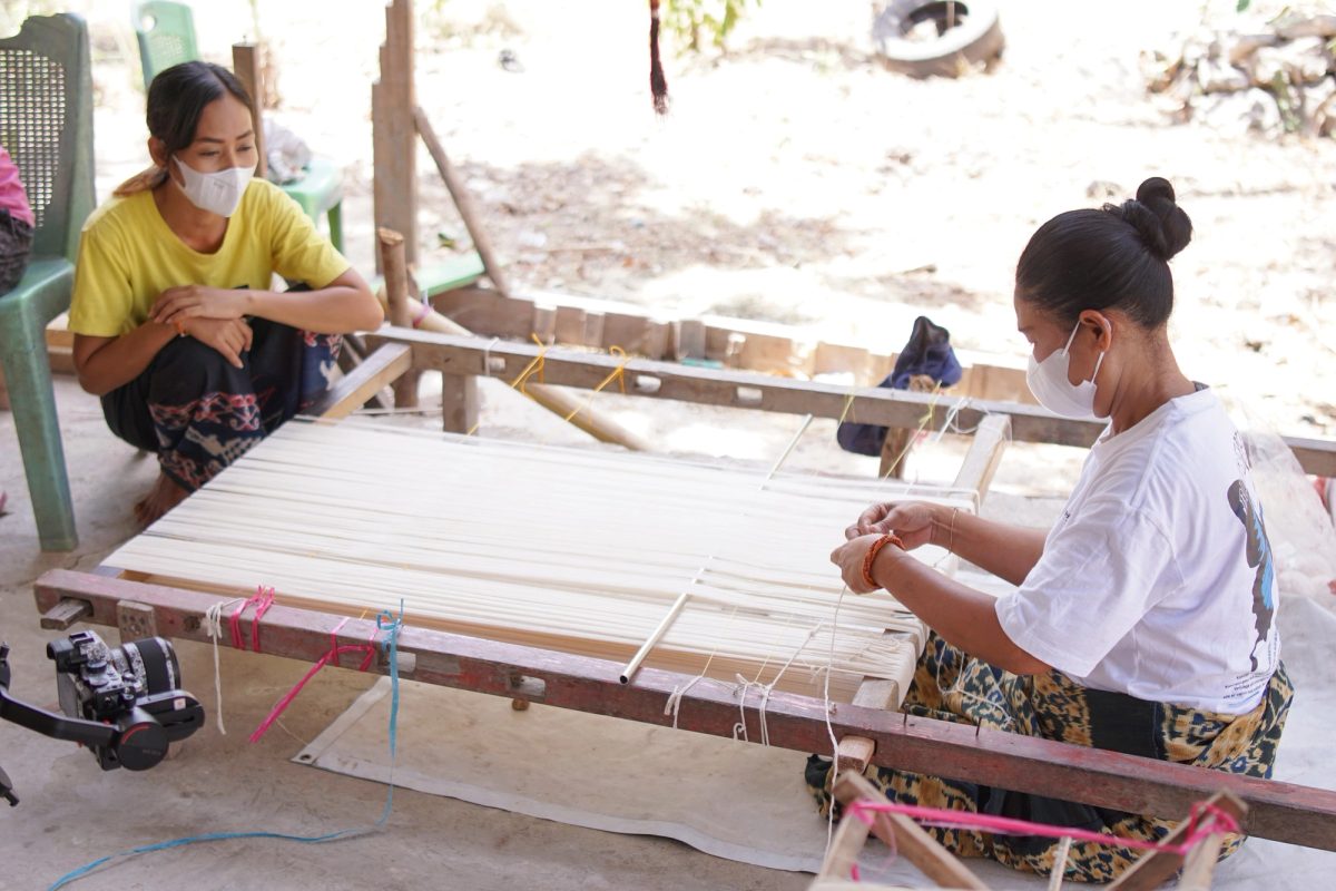 Two women securing groups of white warp threads