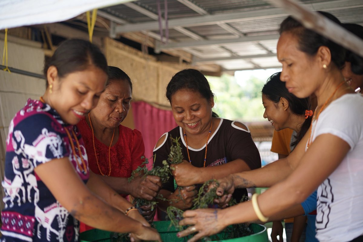 Women smiling as they work indigo leaves together in a green basin