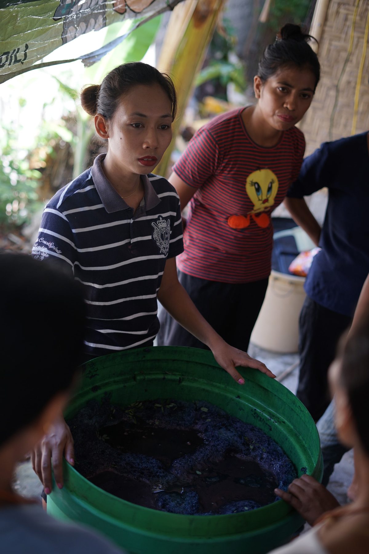 Women handling soaked indigo leaves in a green basin