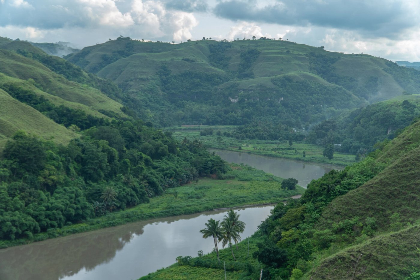 Green Sumba hills and a winding river beneath a cloudy sky