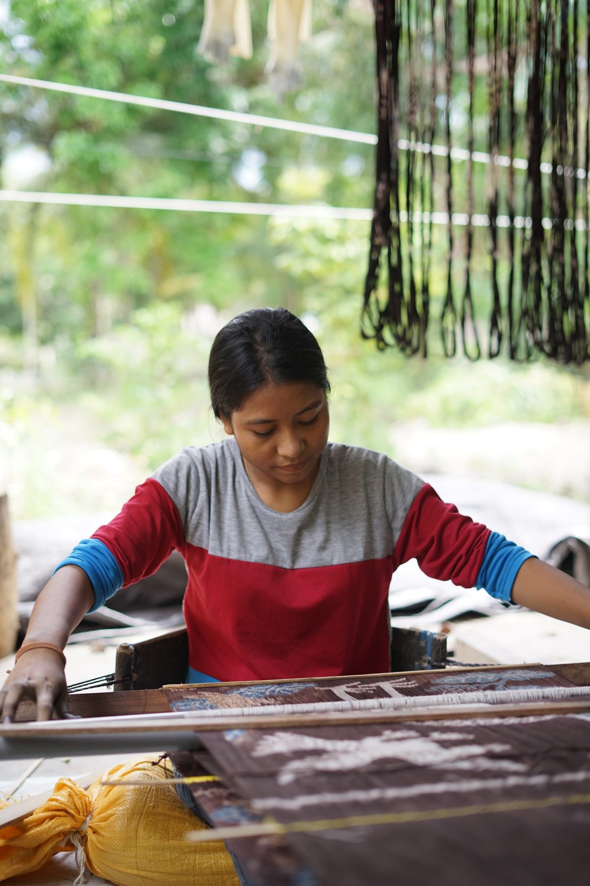 A young woman working at a loom beneath hanging dyed yarn