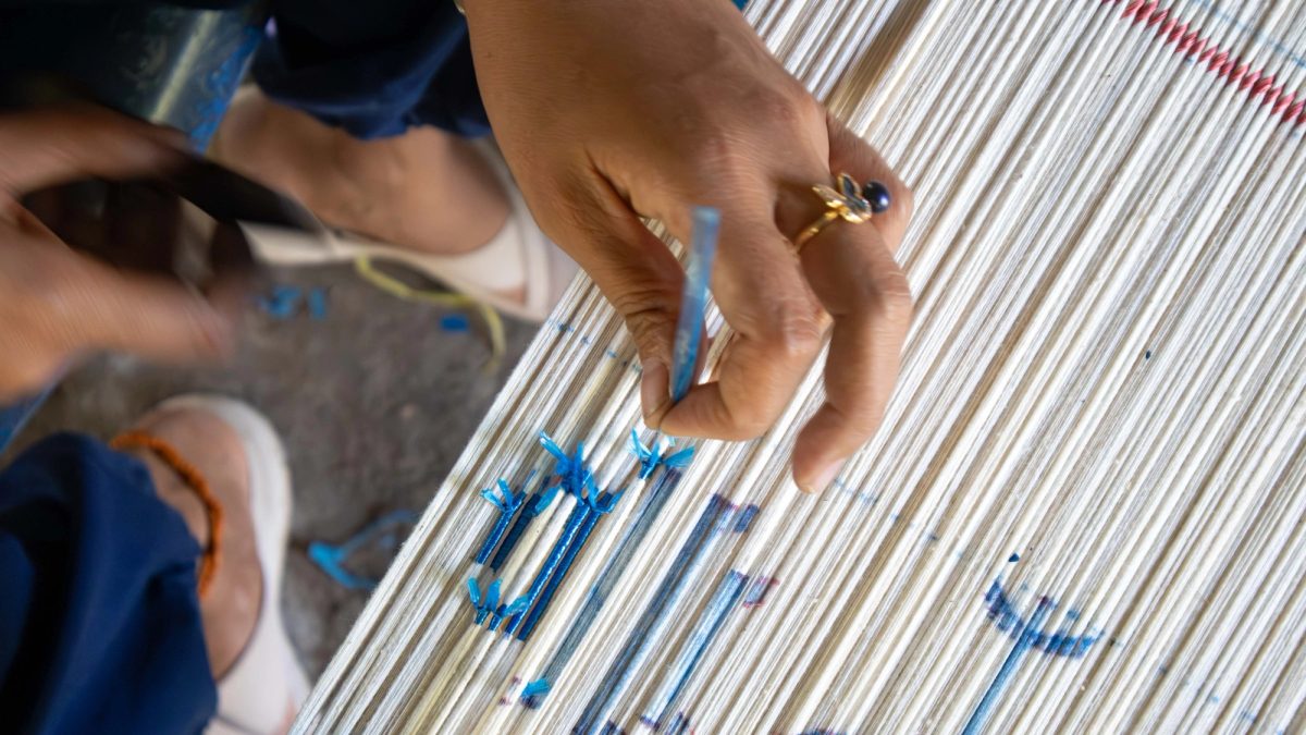 Hands tying blue resist bindings around white threads
