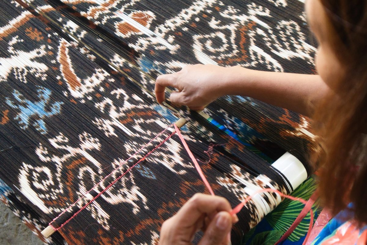 Hands arranging a richly patterned Ikat warp