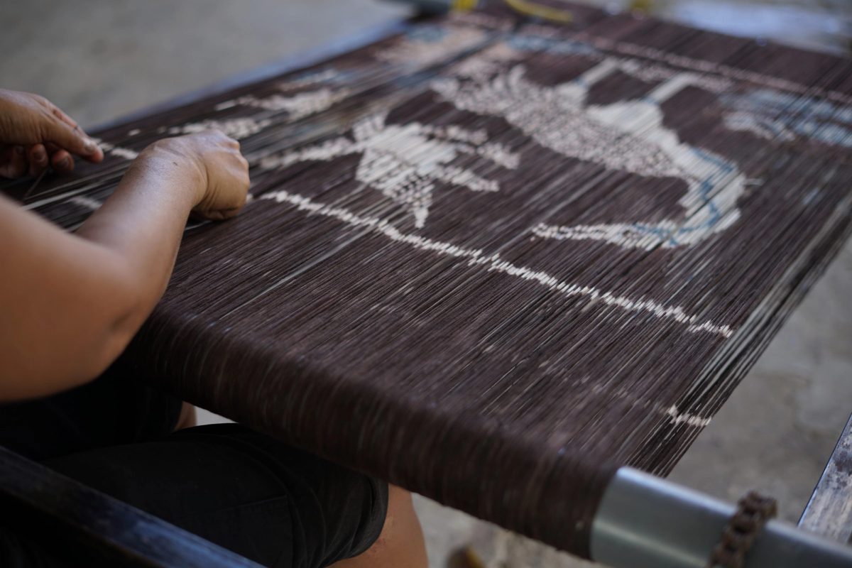 Hands straightening a white motif on dark warp threads