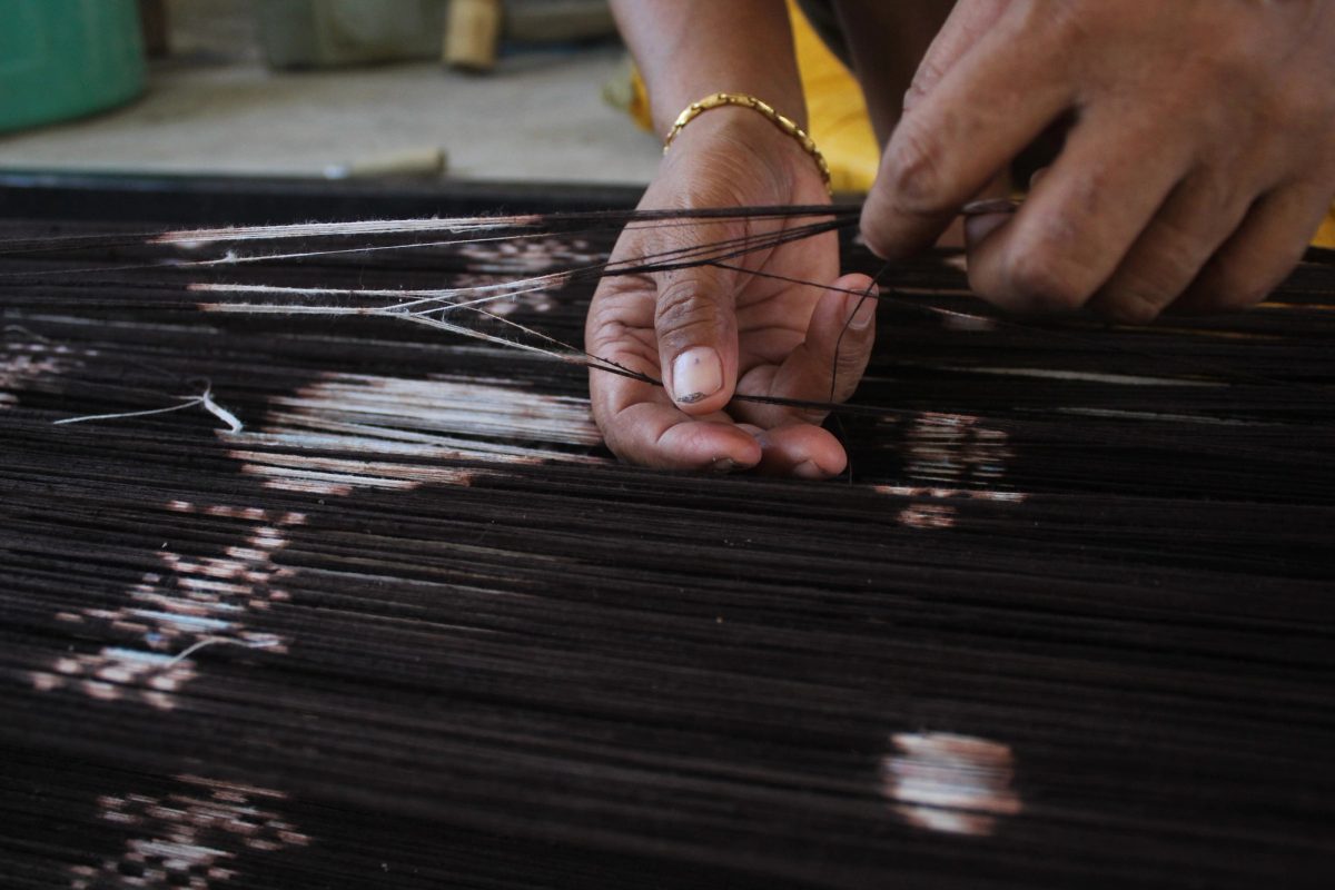 Hands using a fine bamboo tool to separate dark threads