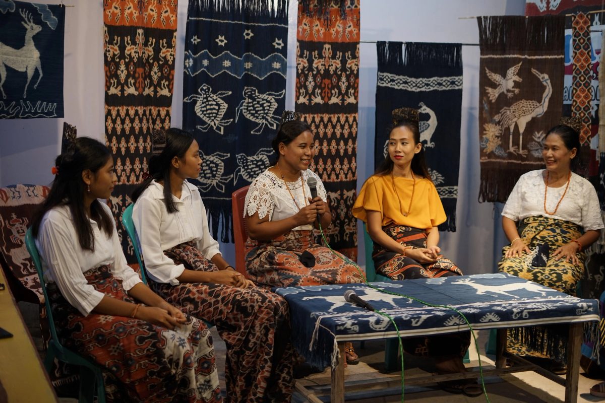 Women sharing a conversation surrounded by displayed Ikat textiles