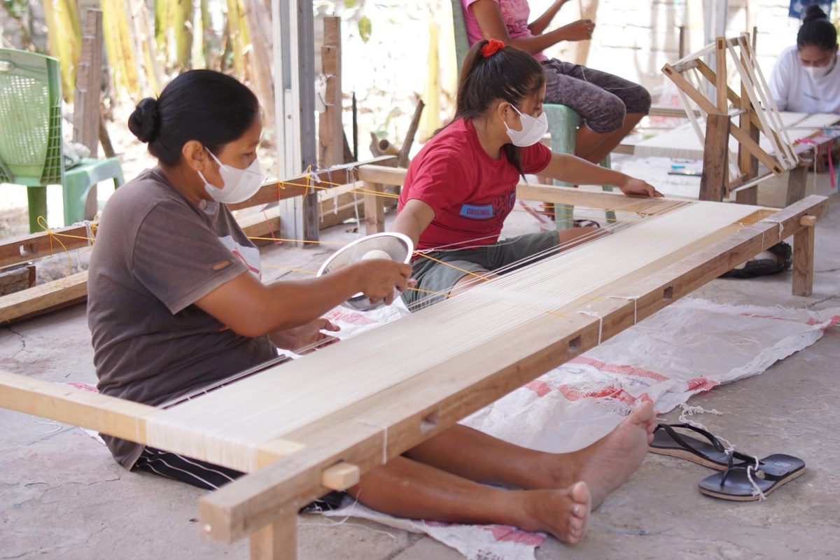 Women arranging white warp threads on a wooden frame