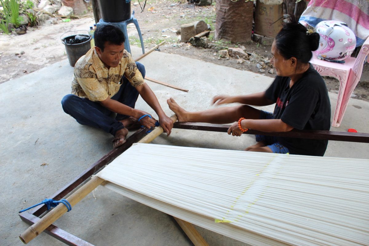 Two women tightening white warp threads on a frame