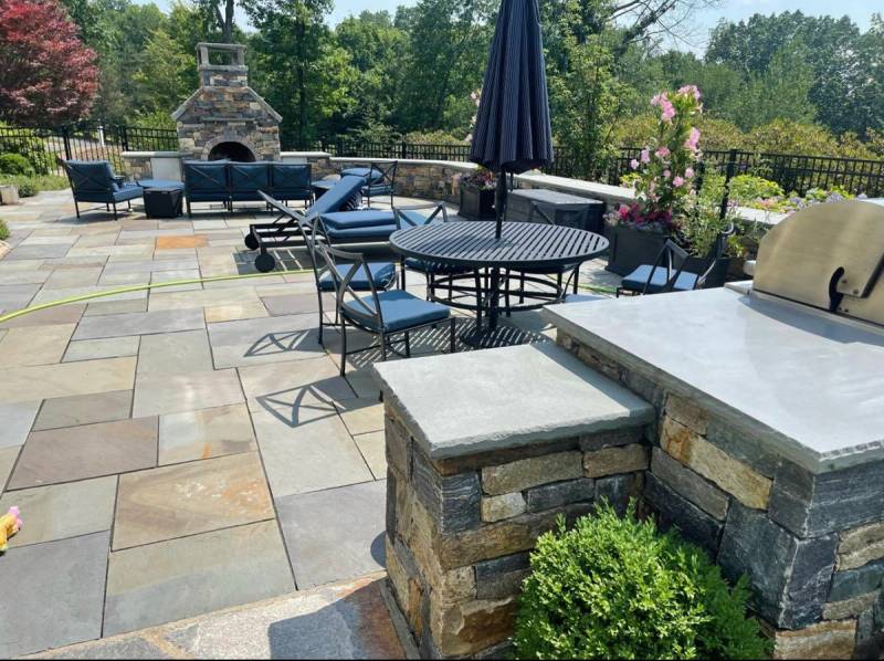 Bluestone patio with outdoor fireplace, stone walls, iron furniture, and built-in grill