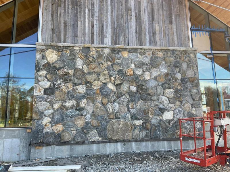 Massive fieldstone veneer wall on modern commercial building with reclaimed wood siding and floor-to-ceiling glass