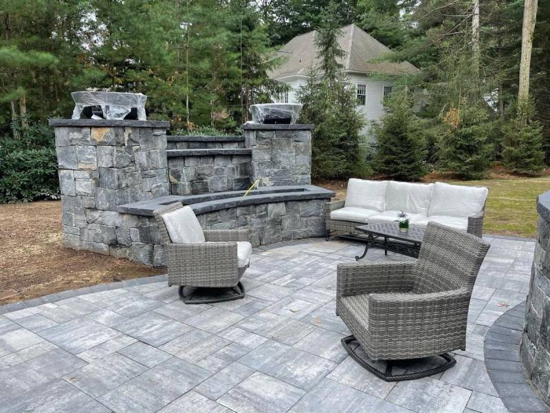 Paver patio with stone fire feature wall, twin pillars, and wicker outdoor furniture
