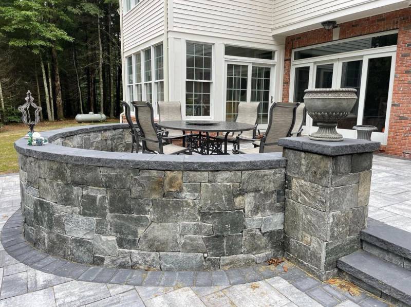 Curved stone seating wall with pillar caps, paver patio, and raised dining area