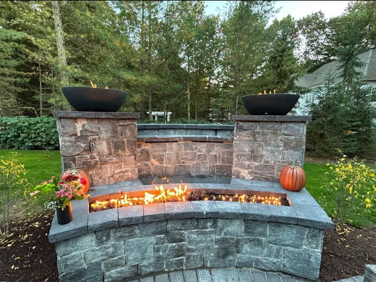 Custom stone fire feature with curved bench, dual fire bowls on pillars, and linear fire trough