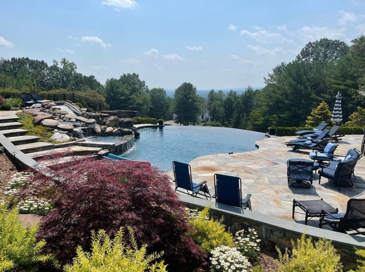 Infinity pool with natural boulder waterfall, flagstone surround, and Japanese maple landscaping