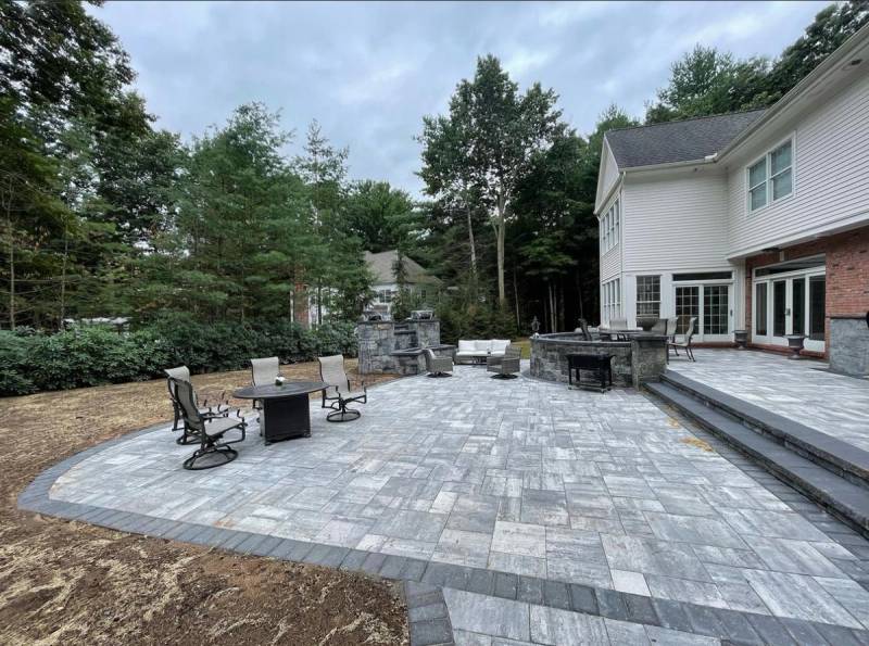Expansive paver patio with stone grill station, furniture, and steps at a colonial home