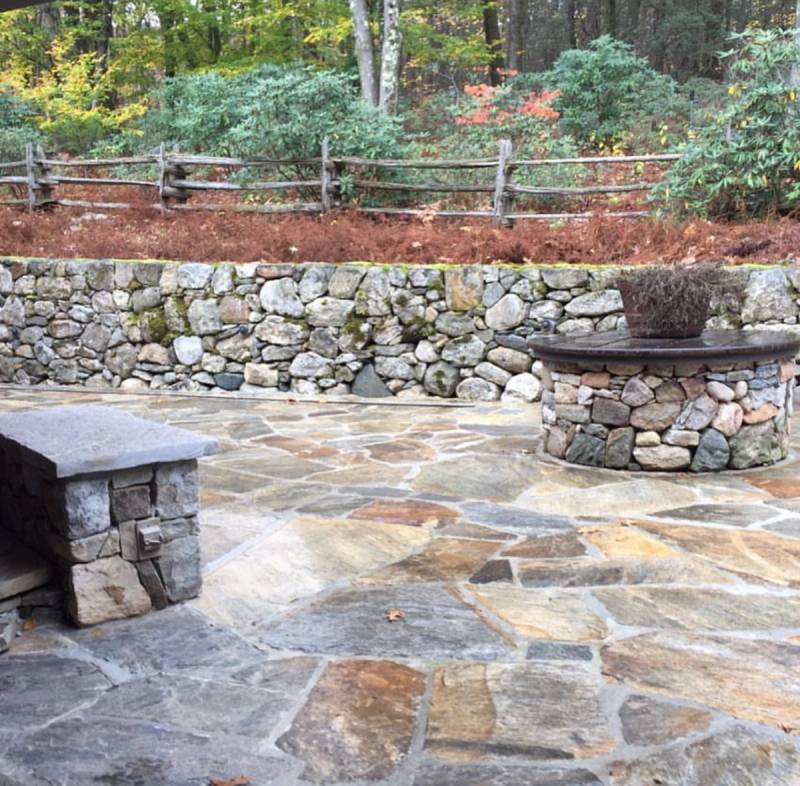 Flagstone patio with natural stone retaining wall and round stone fire pit surrounded by autumn foliage