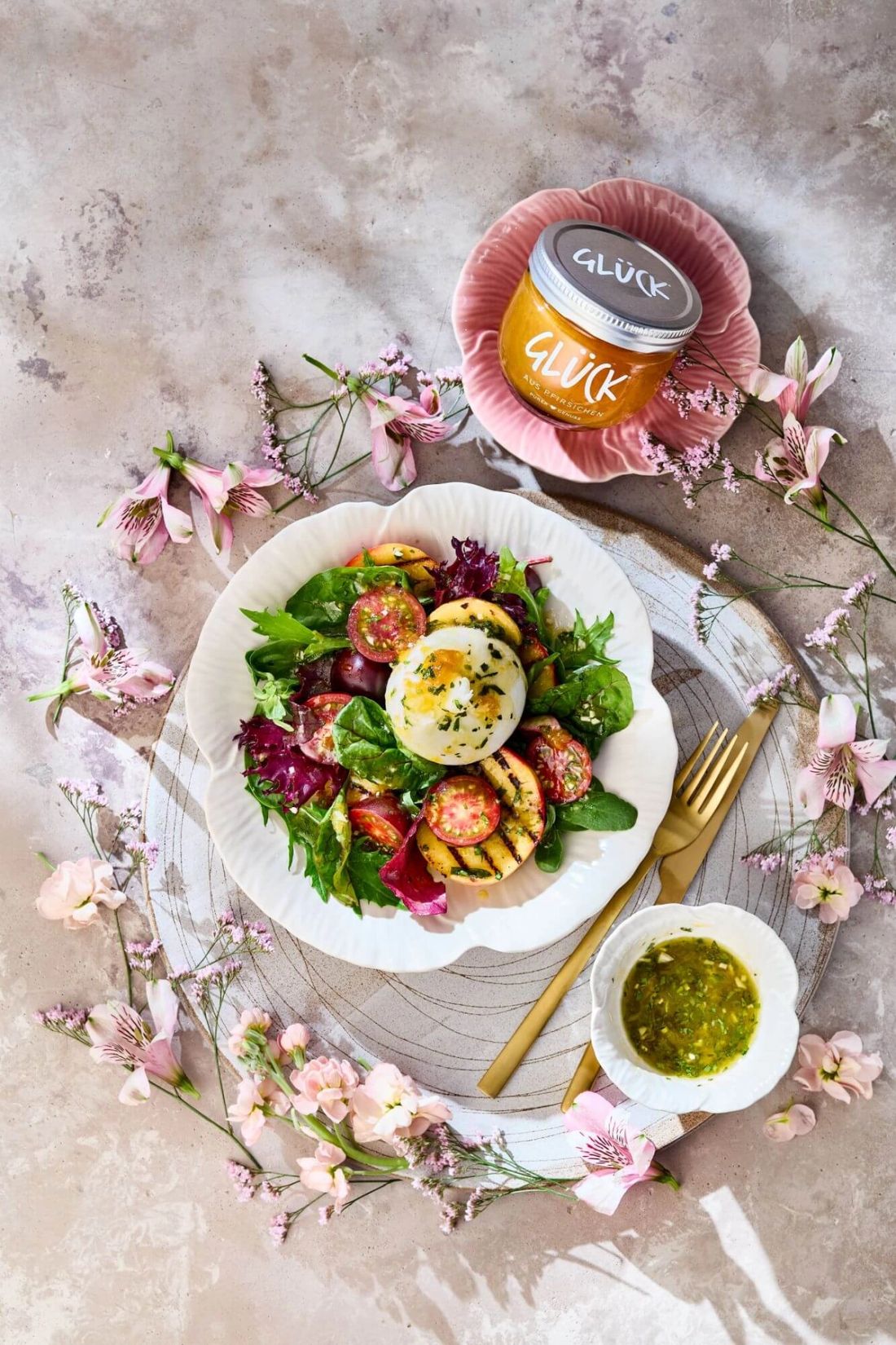 Sommersalat mit Burrata und gegrillten Pfirsichen neben einem Glas GLÜCK aus Pfirsichen.
