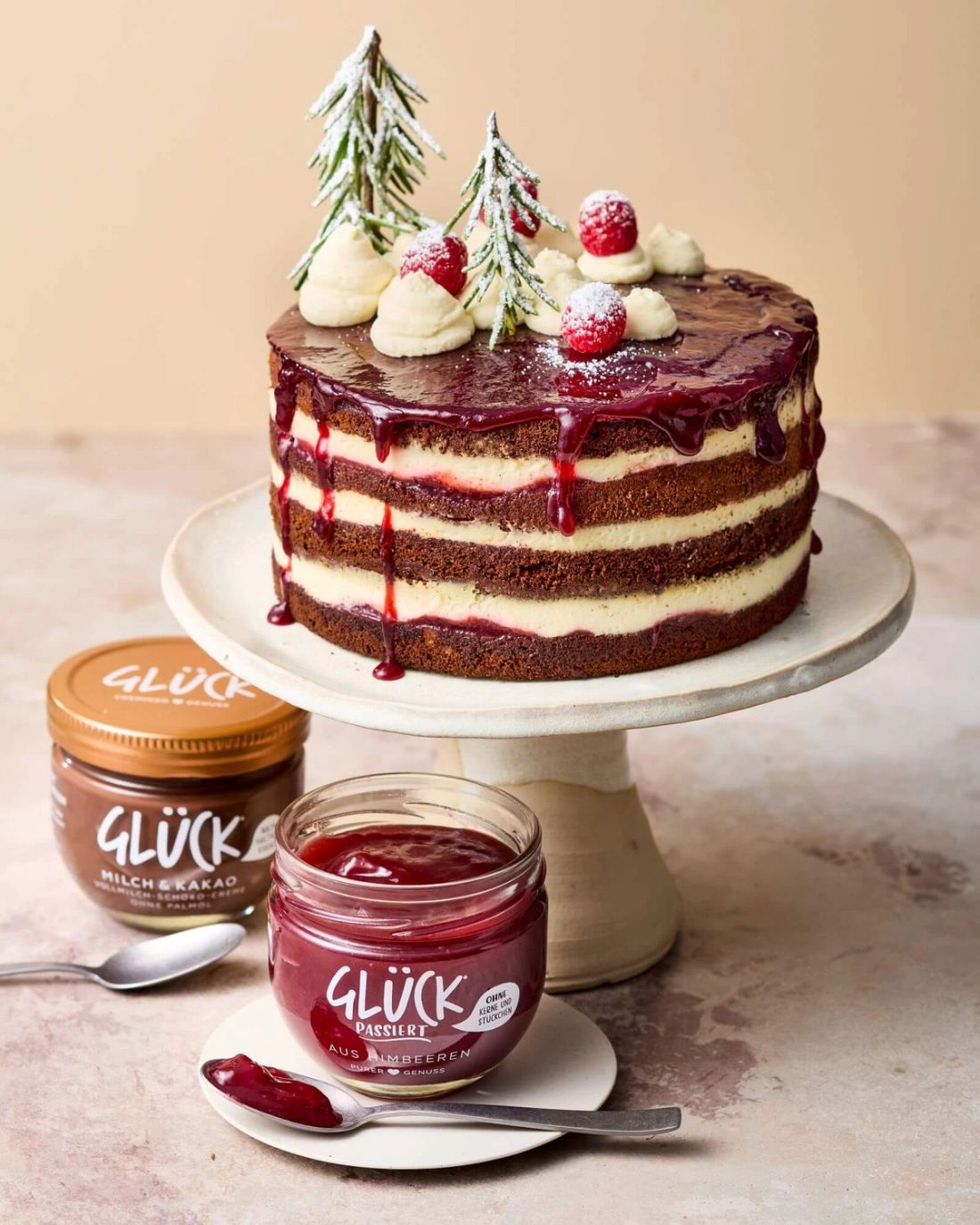Himbeer-Lebkuchen Naked Cake mit Rosmarin-Creme. Daneben je ein Glas GLÜCK Milch & Kakao und GLÜCK passiert aus roten Johannisbeeren.
