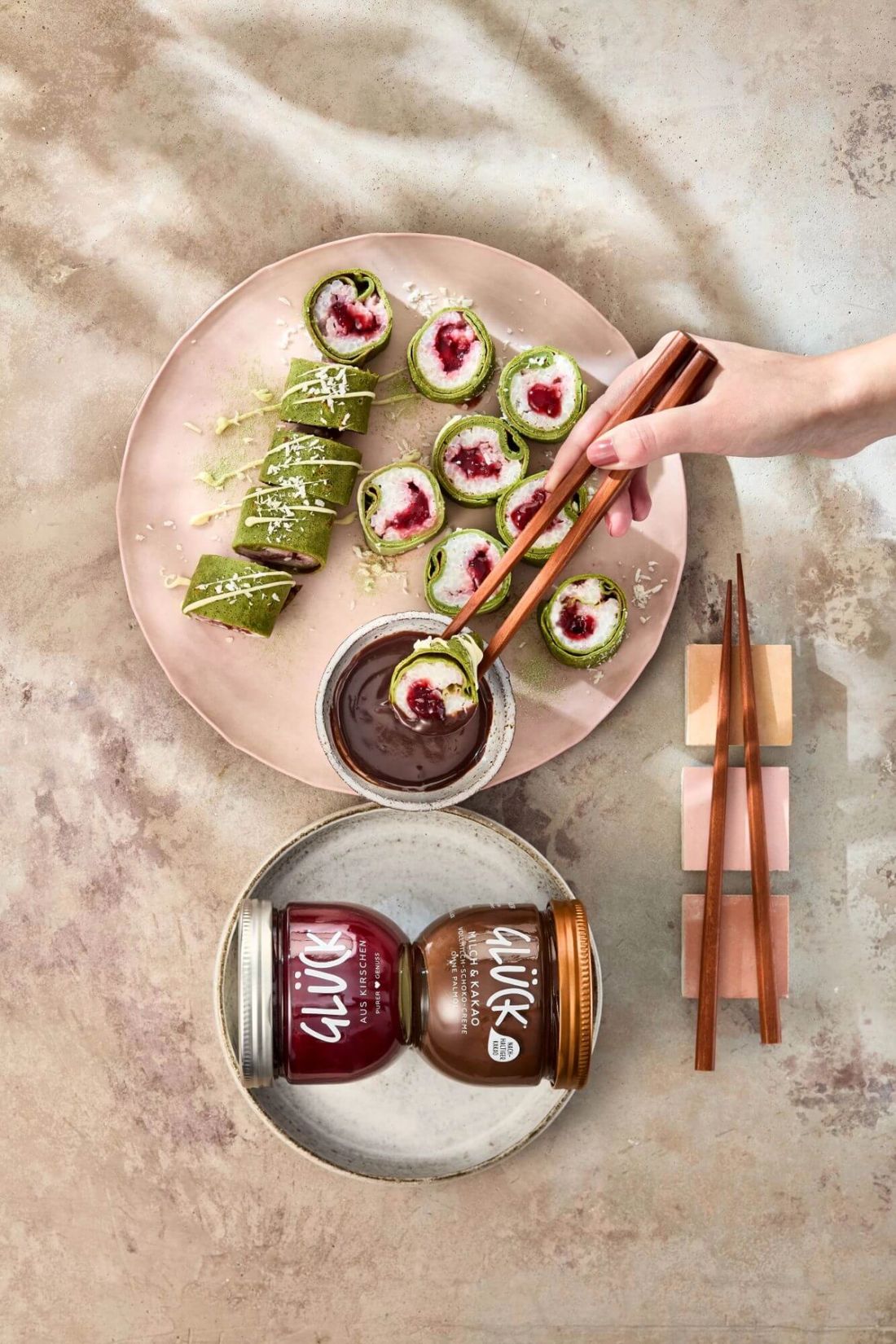 Matcha Milchreis Kirsch-Sushi, angerichtet mit Schokosoße. Daneben je ein Glas GLÜCK Milch & Kakao und GLÜCK aus Kirschen.