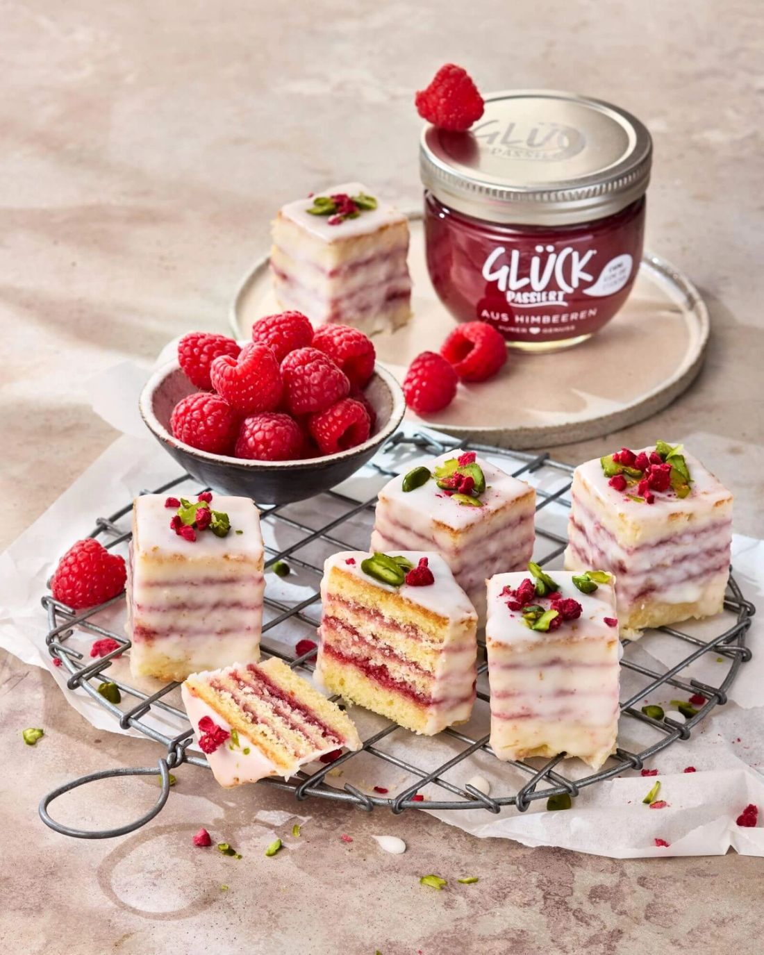 Petit Fours, angerichtet auf einem Teller mit Beeren. Im Hintergrund ein Glas GLÜCK passiert aus Himbeeren.