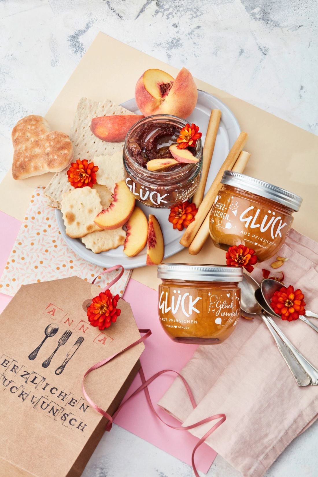 Süßer Pfirsich-Kakao-Hummus im GLÜCK Glas, daneben Cracker, Pfirsiche und zwei Gläser GLÜCK aus Pfirsichen.