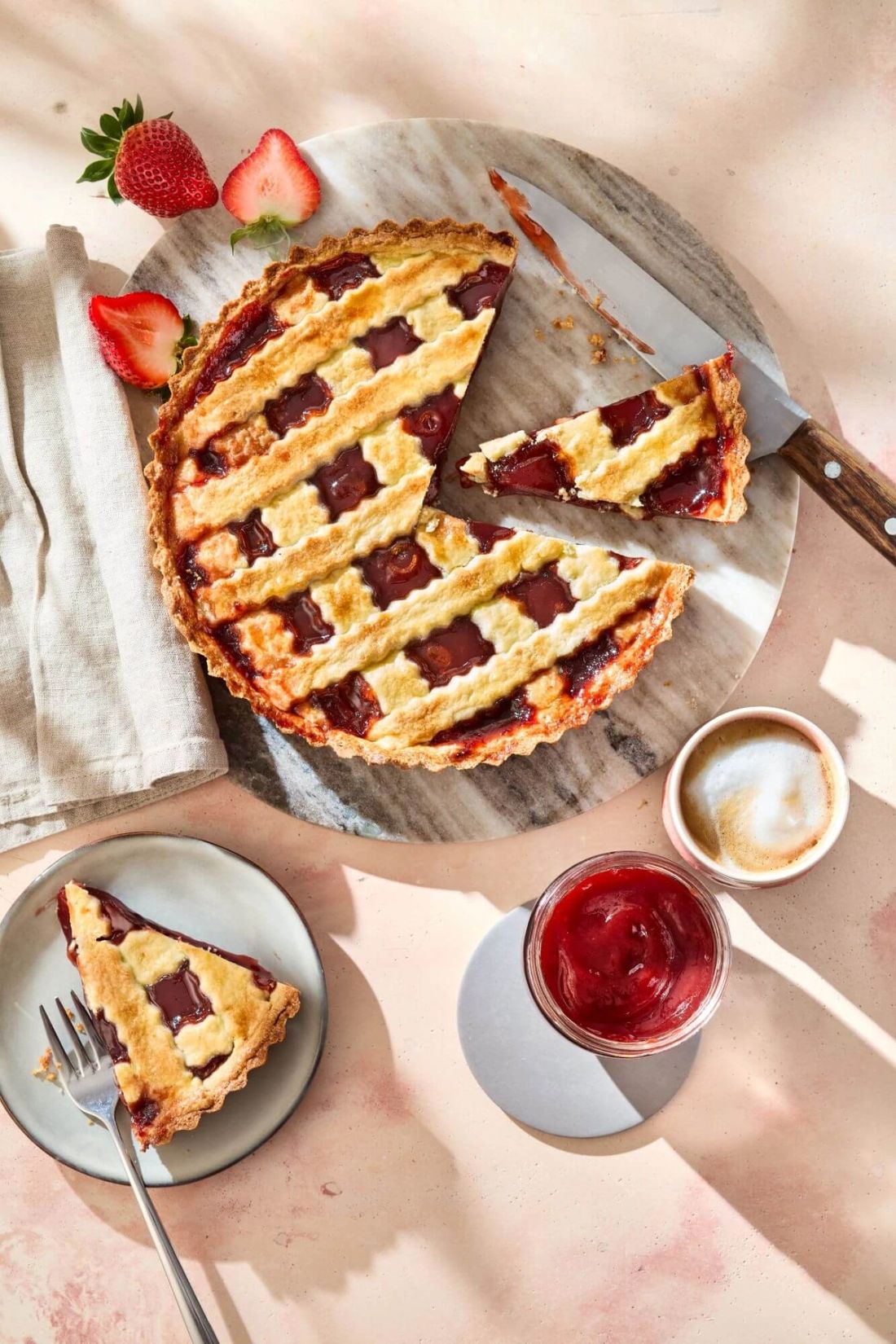 Erdbeer-Crostata, angeschnitten auf einem Brett. Daneben Erdbeersauce und ein Kaffee.