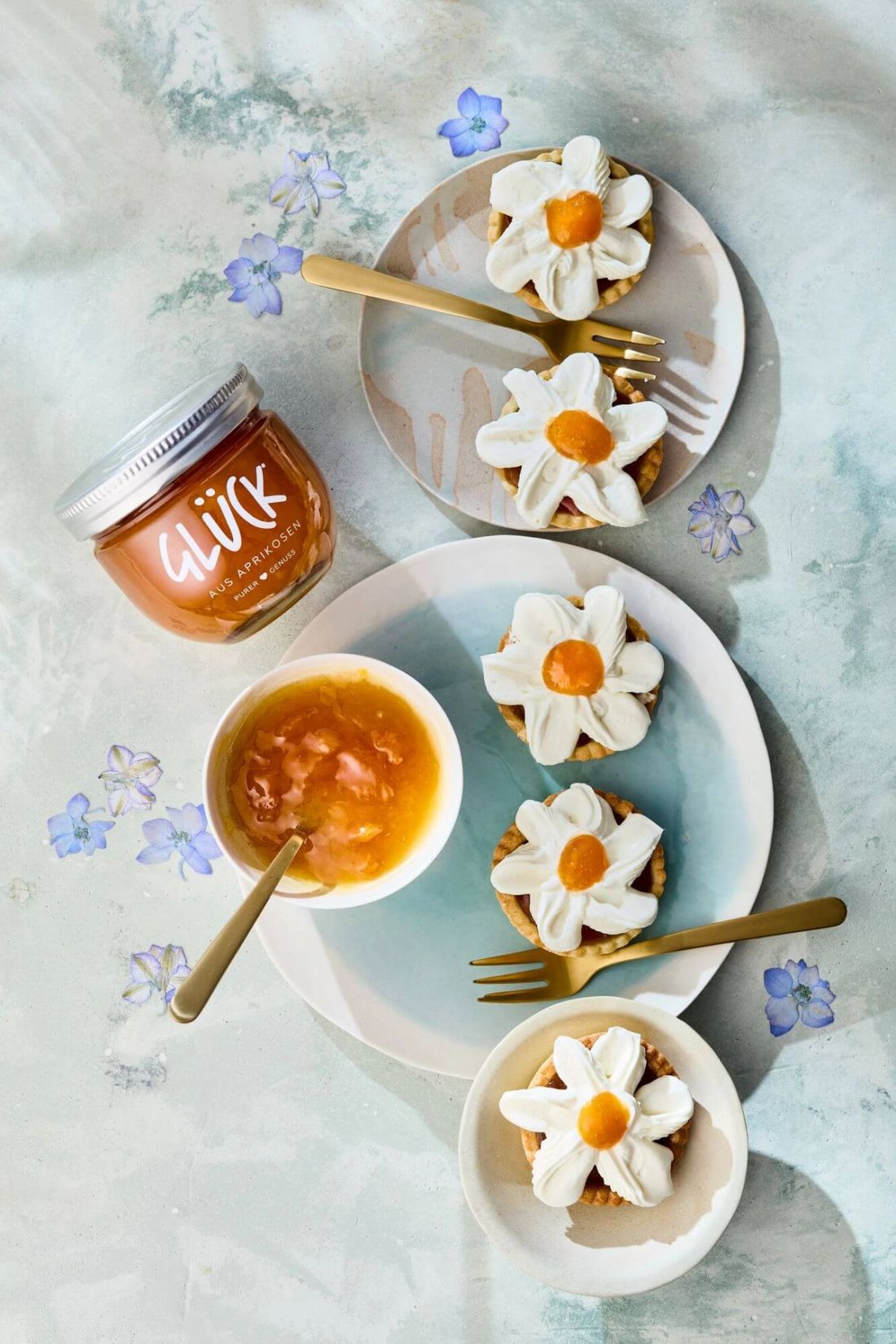 Gänseblümchen Tarteletts auf einem Teller neben einer Aprikosensauce und einem Glas GLÜCK aus Aprikosen.
