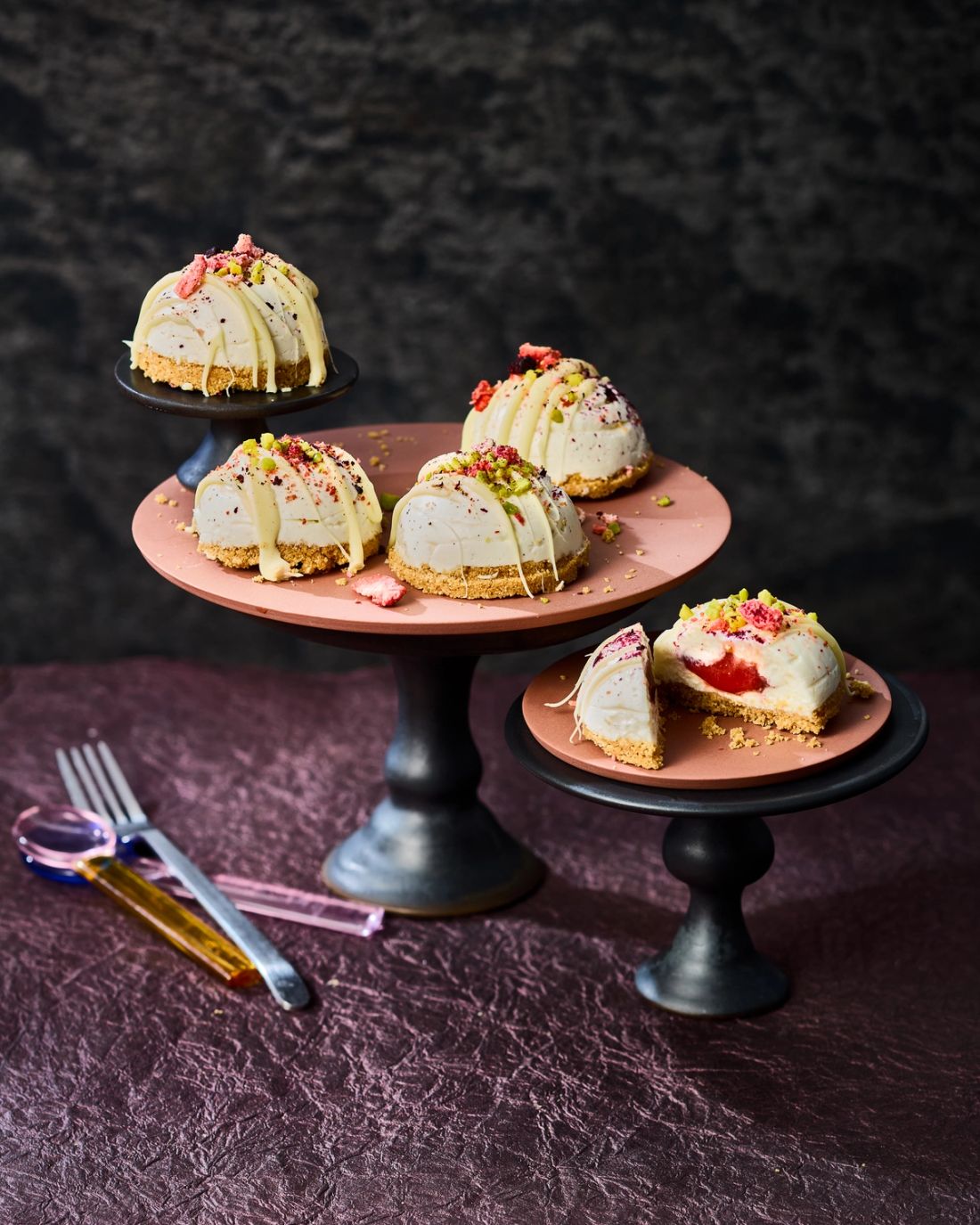 Strawberry Cheesecake Bites, gefüllt mit GLÜCK passiert aus Erdbeeren, angerichtet mit weißer Kuvertüre, Pistazien und Himbeeren.