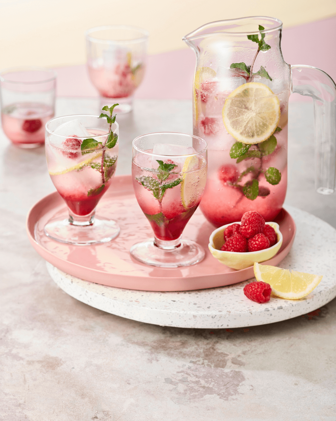 Minz-Himbeer-Limonade mit Zitrone im Glas, daneben eine volle Karaffe. Zur Deko Himbeeren.