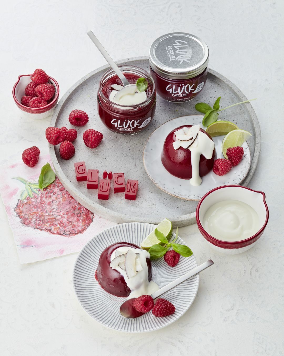 Himbeer Götterspeise, angerichtet mit Kokosjoghurt und Himbeeren. Daneben ein Glas GLÜCK passiert aus Himbeeren.