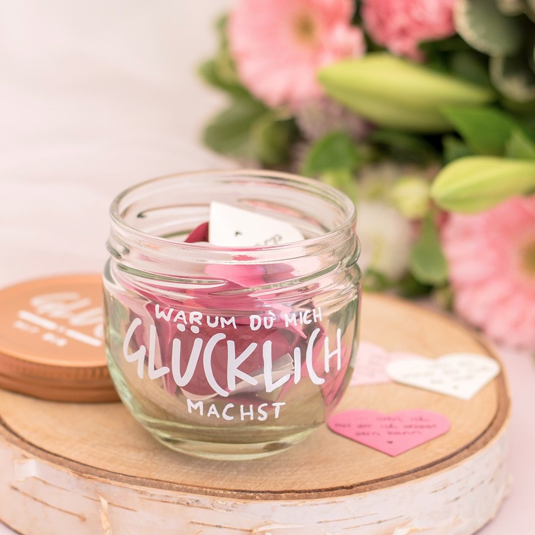 Ein Glas GLÜCK beschriftet mit "Warum du mich glücklich machst". Im Glas und neben dem Glas liegen herzförmige Zettel mit handgeschriebenen Botschaften.