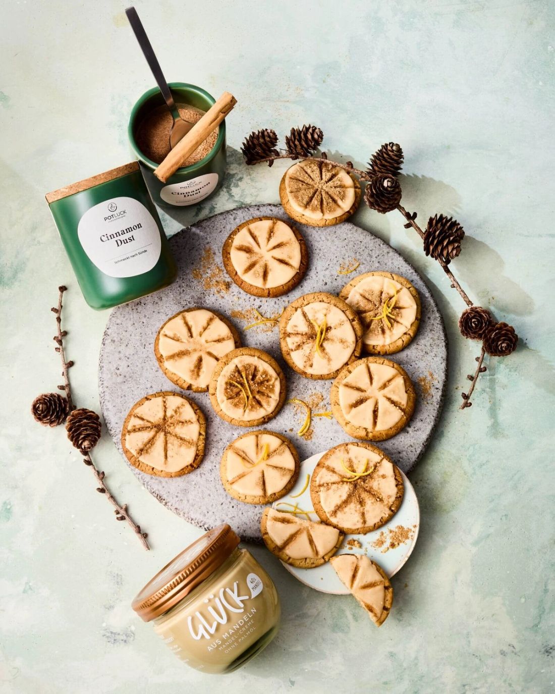 Cinnamon Dust Chai Cookies auf einem Teller. Daneben ein Glas GLÜCK aus Mandeln und ein Topf Potluck Cinnamon Dust.