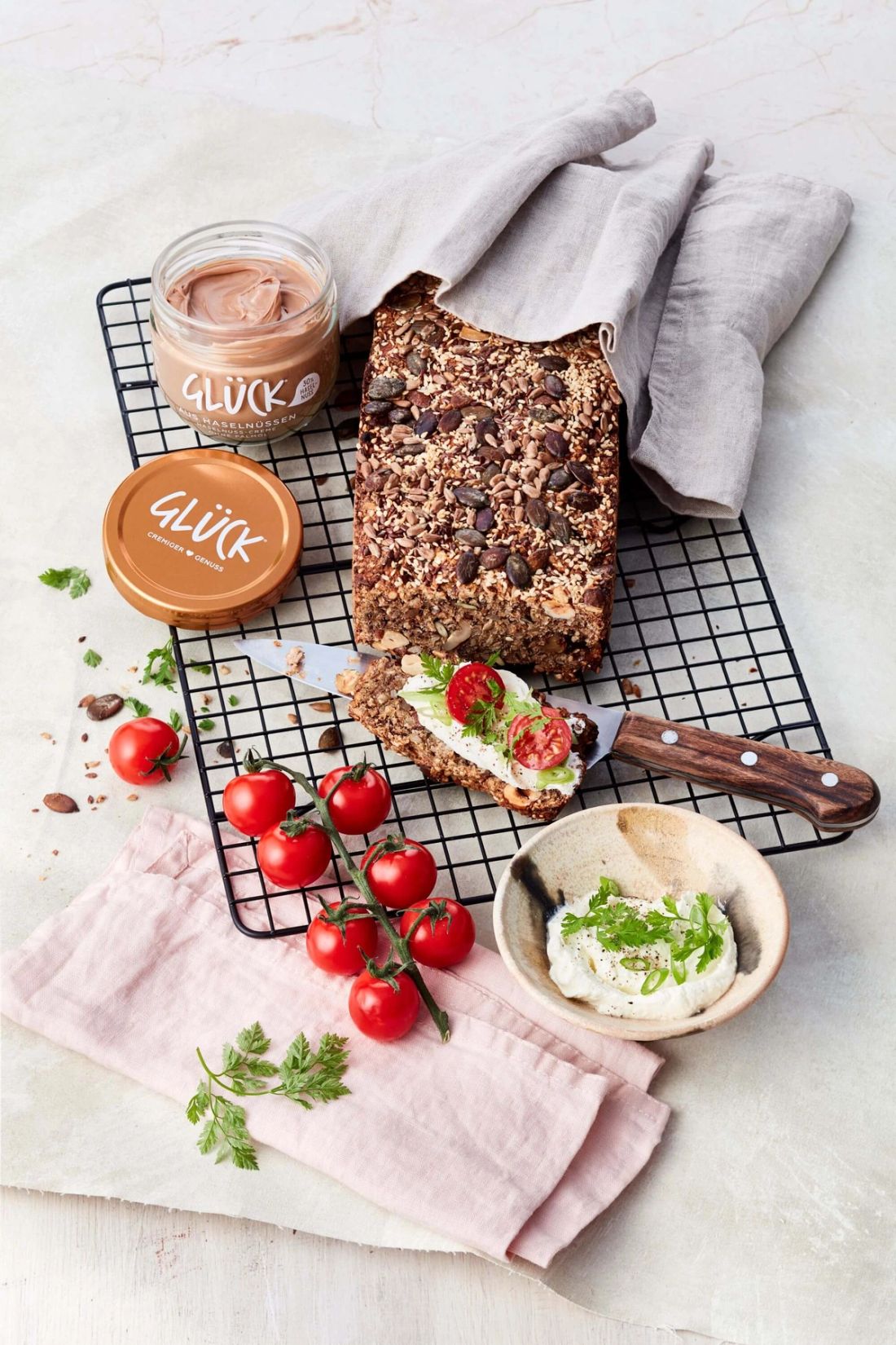 Haselnuss-Körnerbrot, garniert mit einer Creme und Tomaten. Daneben ein Glas GLÜCK aus Haselnüssen.