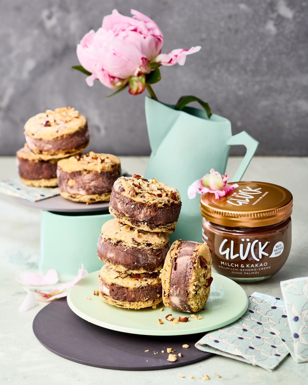 Cookie-Eis-Sandwiches gestapelt auf einem Teller. Daneben ein Glas GLÜCK Milch & Kakao.