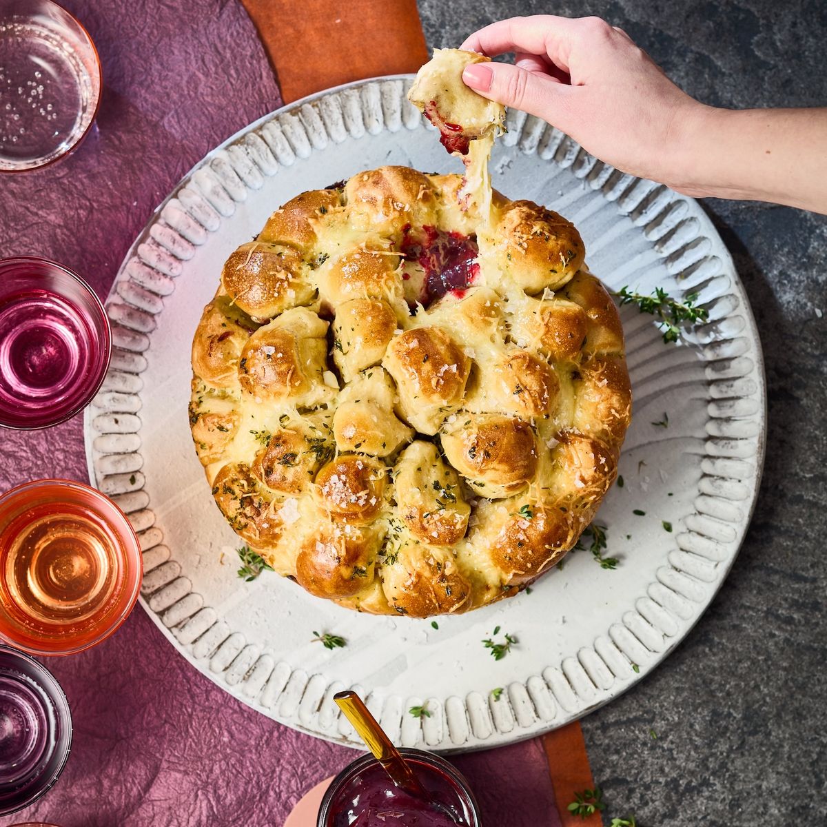 Bewegtbild eines Laugen-Monkey-Bread Rezeptes bei dem drei Hände nacheinander ein Stück vom Brot rausziehen. Dies ist mit Marmelade gefüllt.
