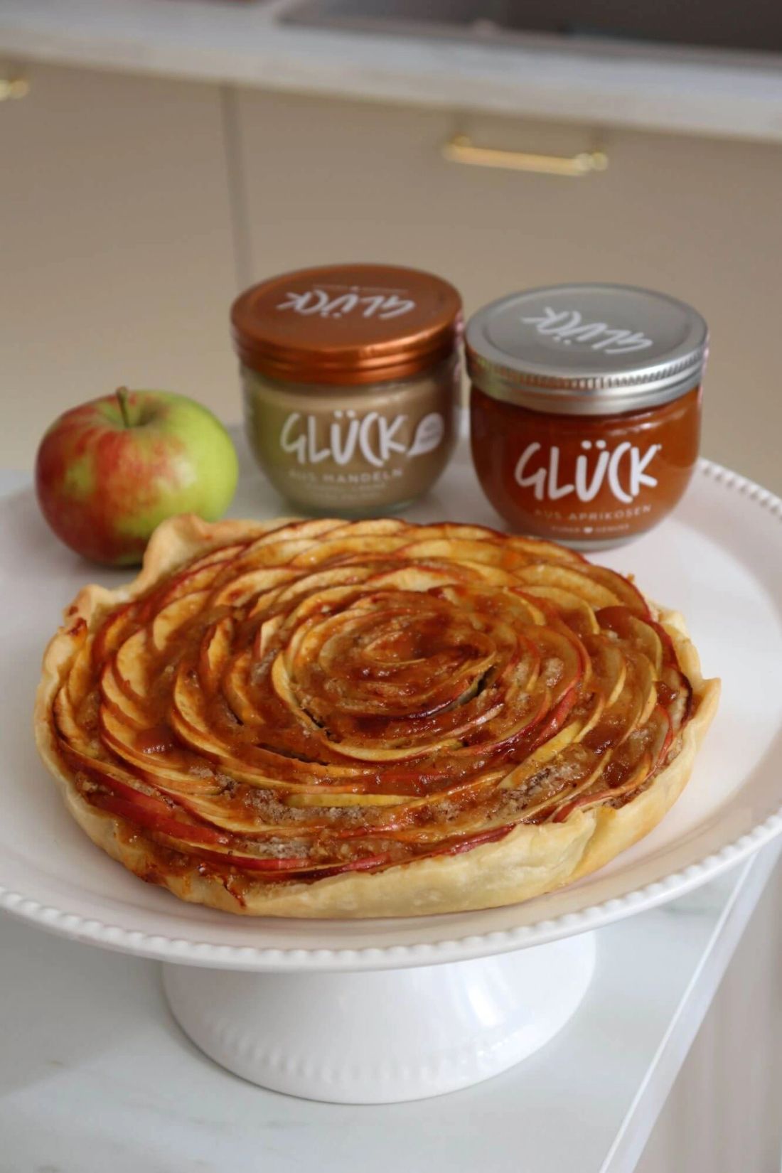 Apfeltarte. Dahinter ein Glas GLÜCK aus Mandeln und ein Glas GLÜCK aus Aprikosen.