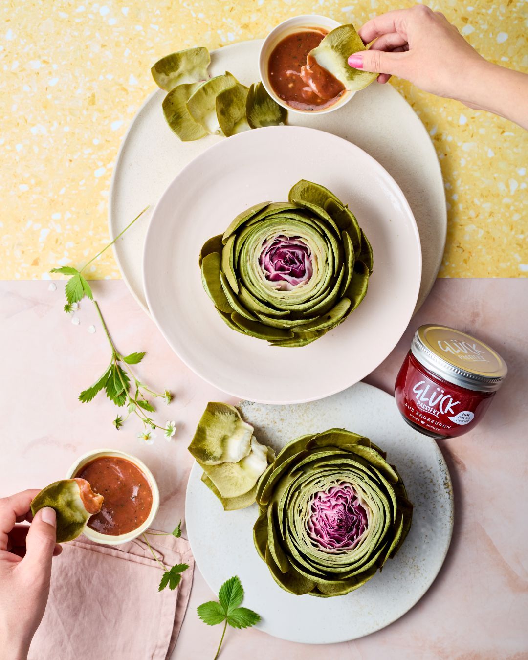 Artischocken mit Erdbeer-Senf-Dressing mit GLÜCK passiert aus Erdbeeren. Zwei Hände dippen Artischocken in das Dressing.