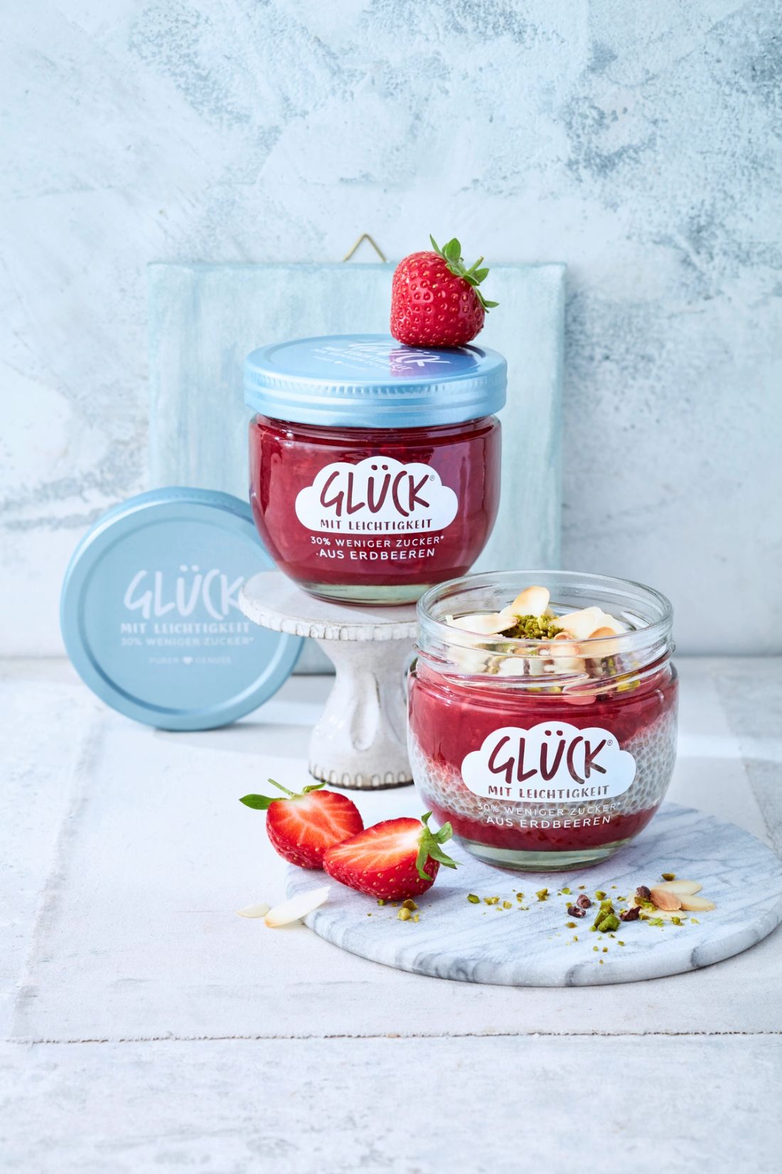 Erdbeer-Chia-Pudding mit Knuspertopping im GLÜCK Glas, daneben GLÜCK mit Leichtigkeit aus Erdbeeren.