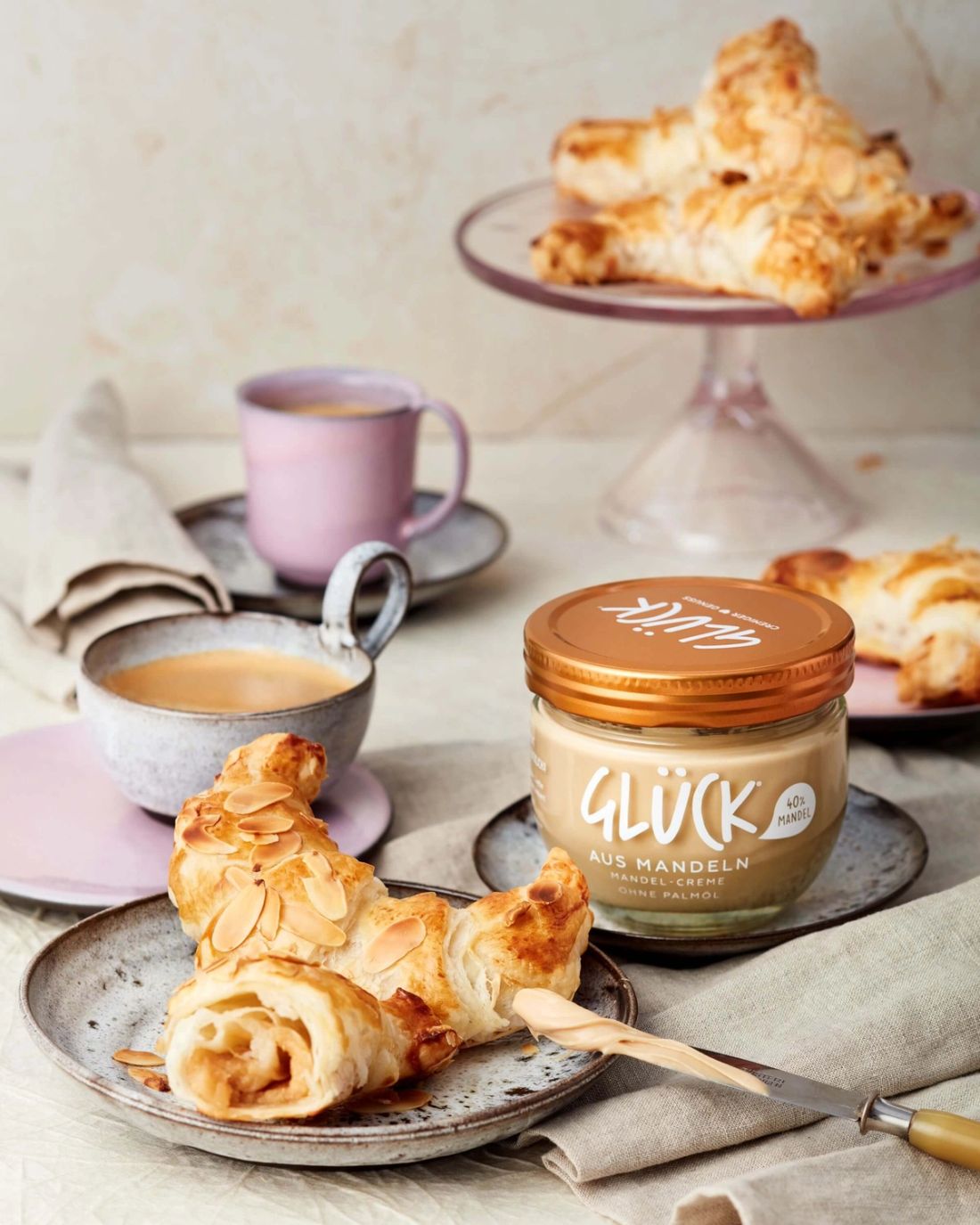 Blitz Mandelcroissants auf einem Teller. Daneben ein Glas GLÜCK aus Mandeln.