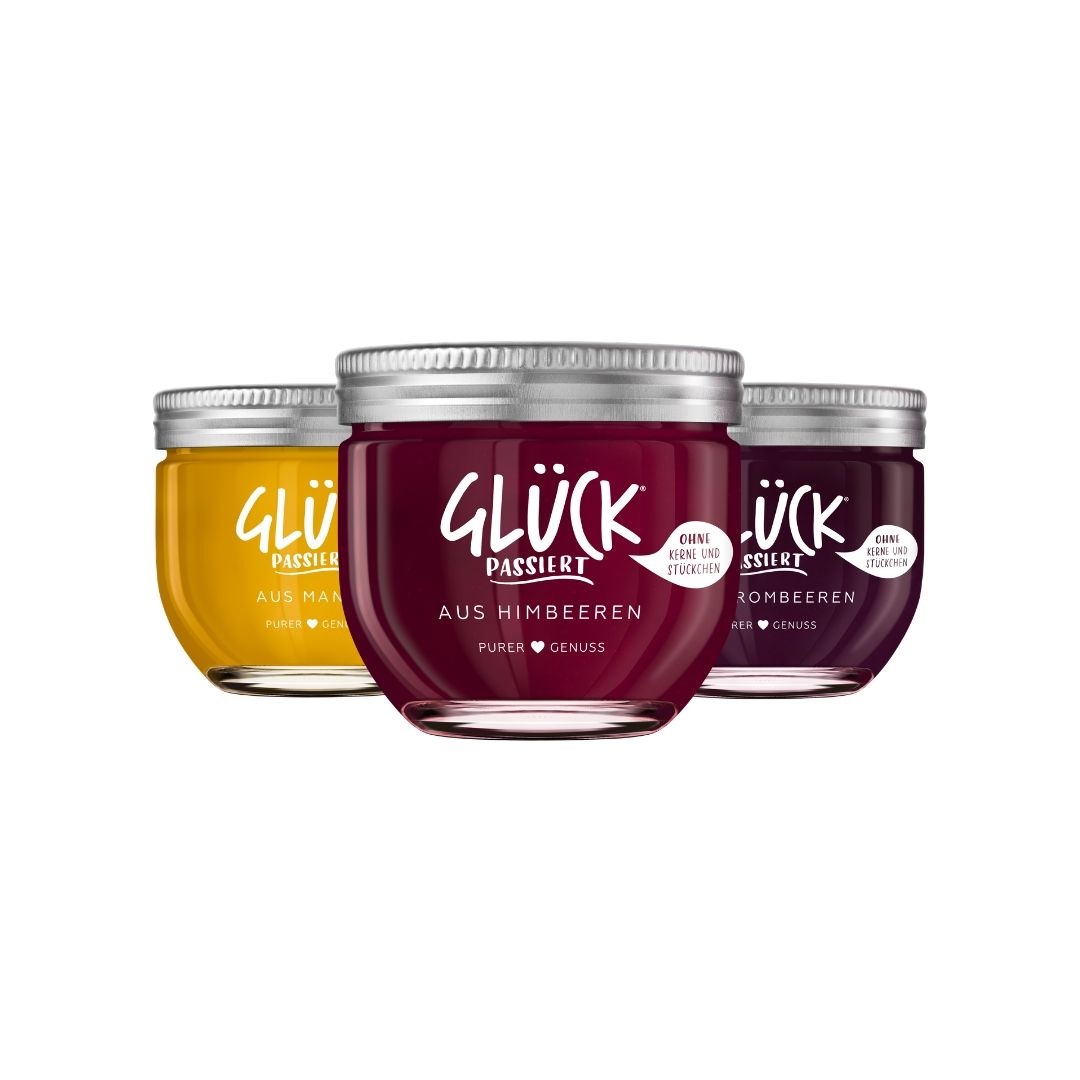 Zu sehen sind drei Sorten der passierten GLÜCK Range: GLÜCK passiert aus Himbeeren, GLÜCK passiert aus Brombeeren und GLÜCK passiert aus Mango.