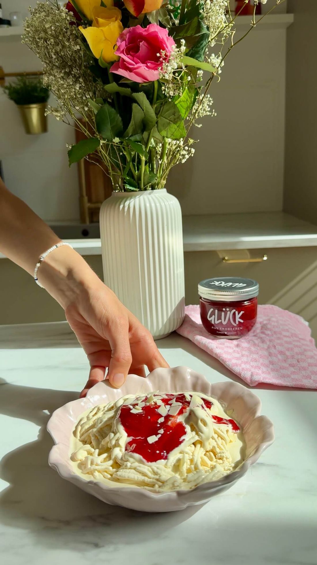 GLÜCK Spaghetti-Eis in einer Schüssel vor einem Glas GLÜCK aus Erdbeeren.