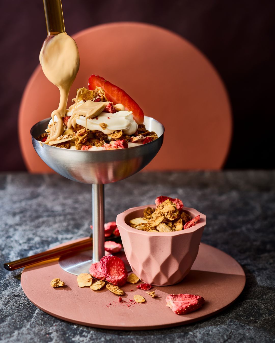 Mandel-Granola mit Erdbeeren in einer Schüssel, garniert mit Erdbeeren und GLÜCK aus Mandeln.