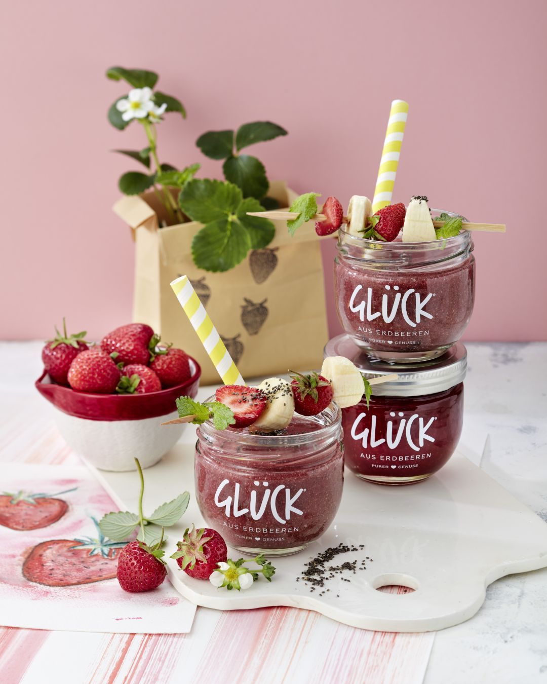 Erdbeer-Chia-Smoothie serviert in einem leeren Glas GLÜCK aus Erdbeeren. Garniert mit Erdbeer-Banane-Fruchtspießen.